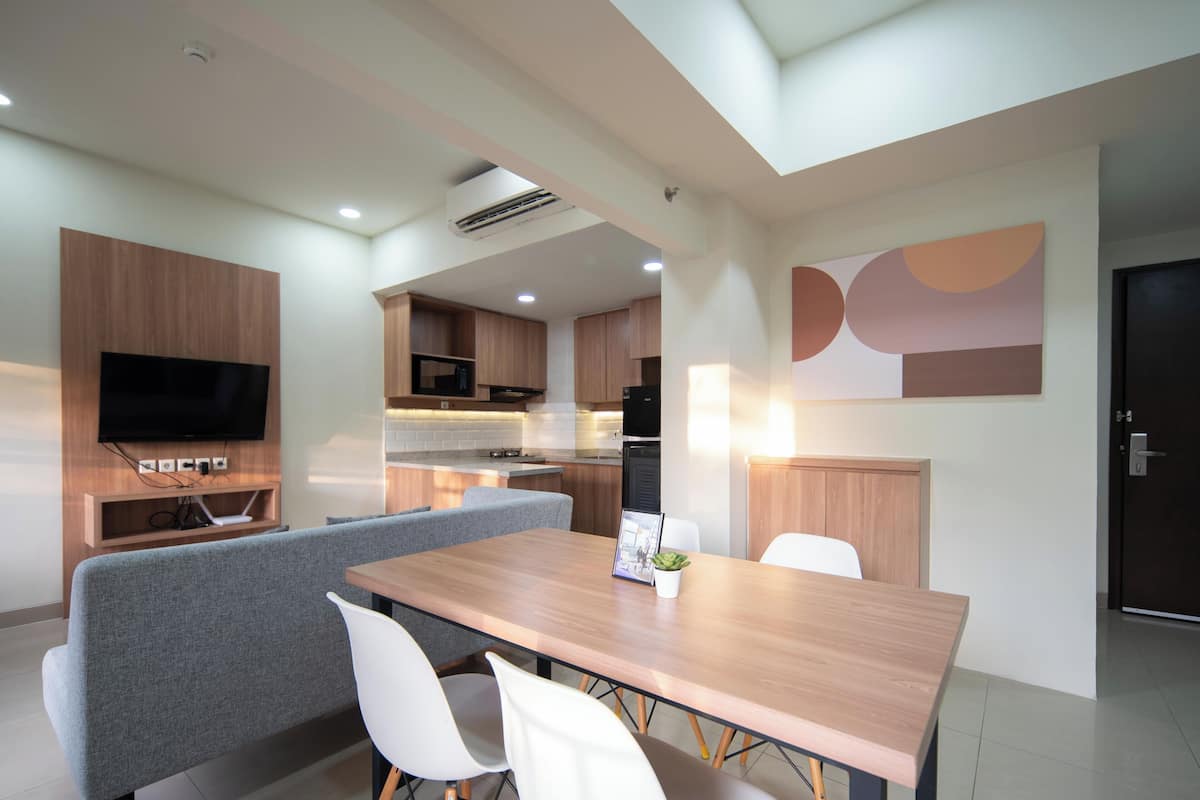 A modern kitchen with built-in appliances, a dining area with a wooden table and white chairs, and a flat-screen TV mounted on the wall.