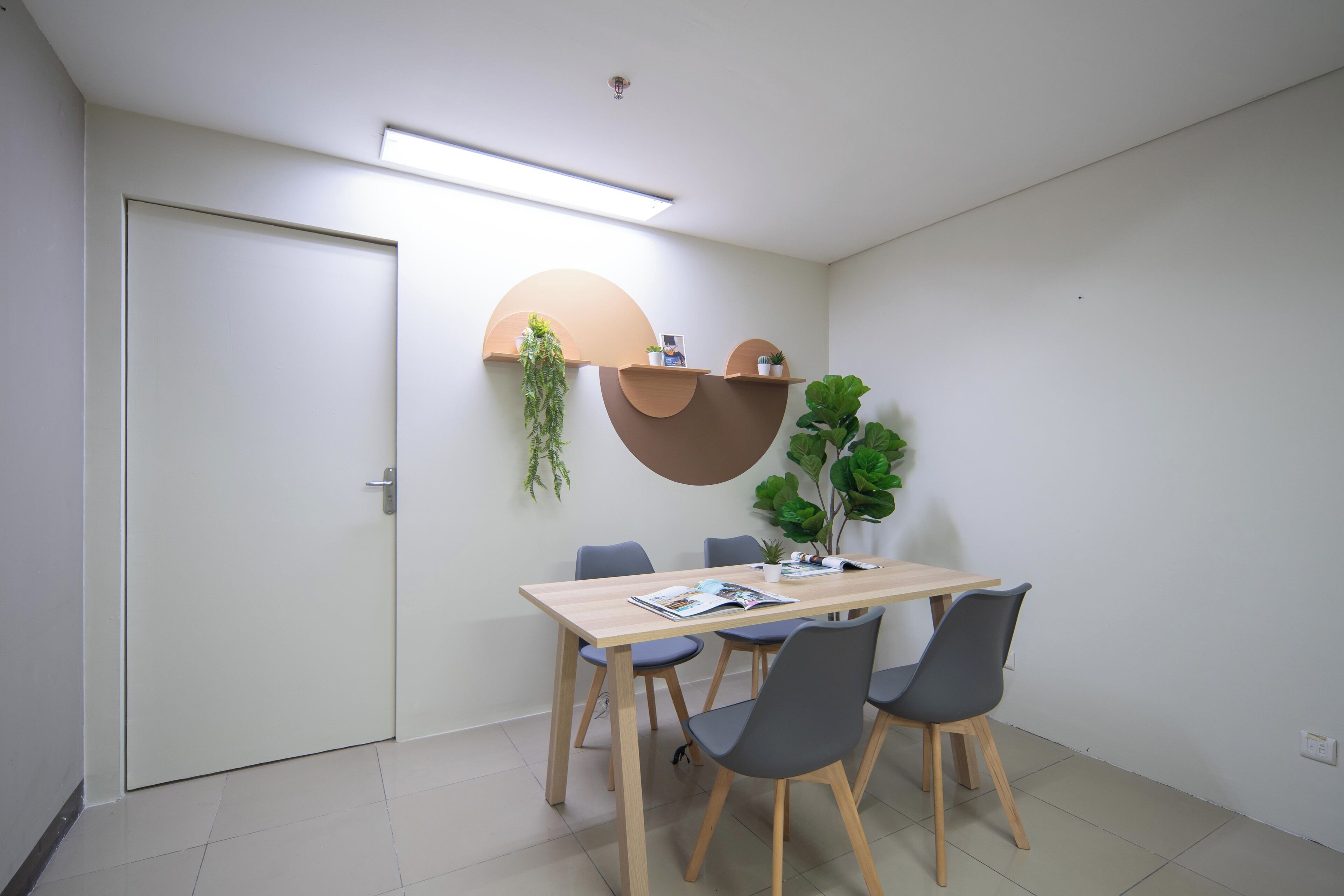 Una sala de reuniones moderna con una mesa de madera, cuatro sillas, una puerta blanca y estanterías fijas con plantas.