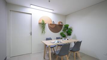 Una sala de reuniones moderna con una mesa de madera, cuatro sillas, una puerta blanca y estanterías fijas con plantas.