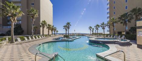 A swimming pool with a sunburst effect, surrounded by palm trees and lounge chairs, with a high-rise building in the background.