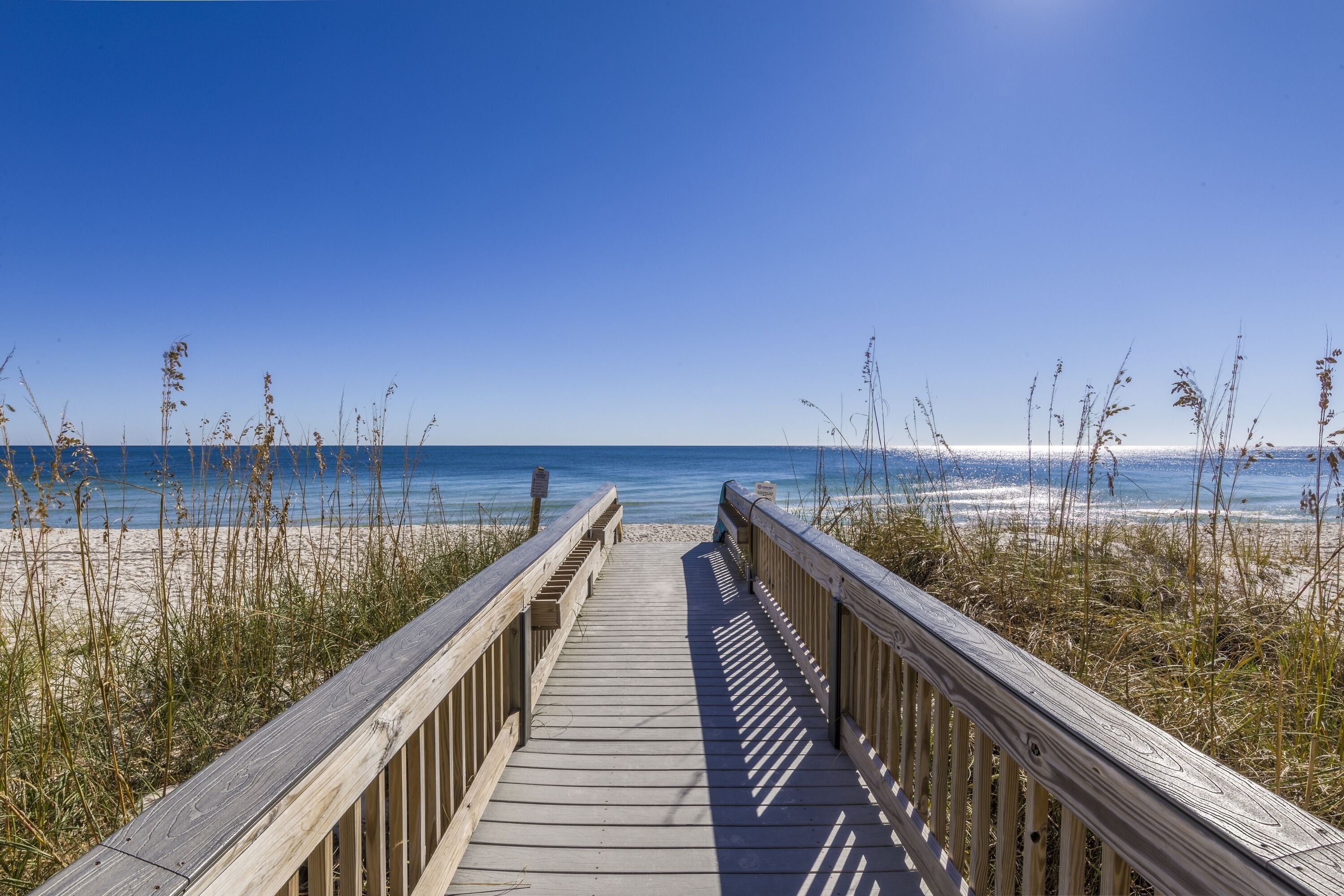 A wooden boardwalk leading to a beach with clear skies.