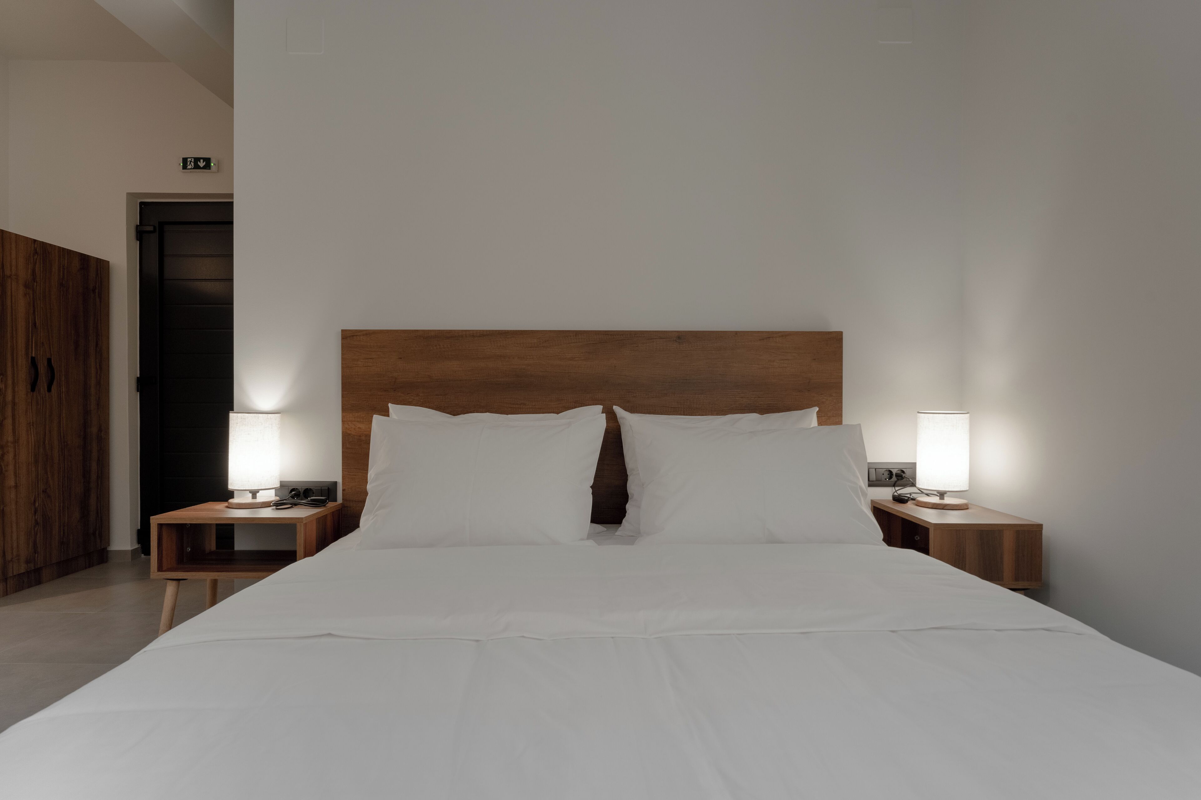 A hotel room with a large bed, wooden headboard, two bedside tables with lamps, and a wardrobe.