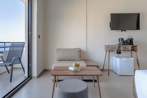 A modern living room with a sofa, a coffee table, a small ottoman, a TV, and a mini-fridge.