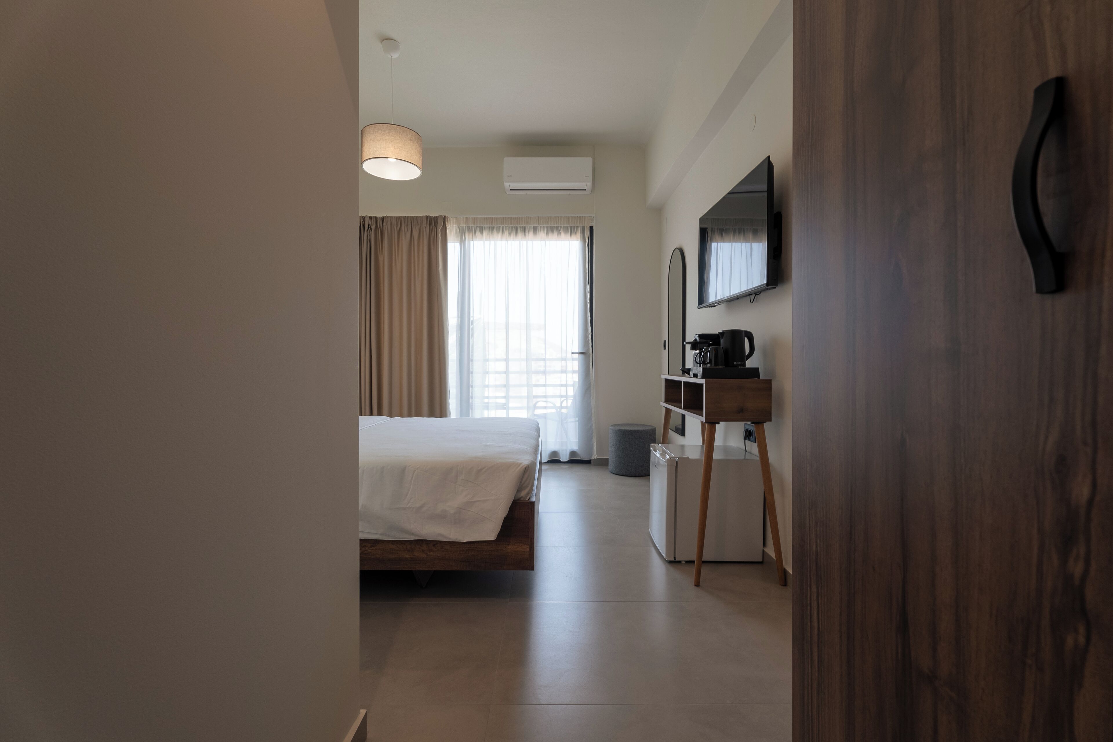A modern hotel room with a bed, a desk, a mirror, and a television.