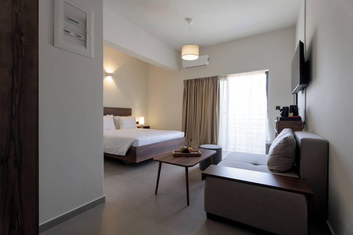 A hotel room with a bed, a sofa, a coffee table, and a TV mounted on the wall.