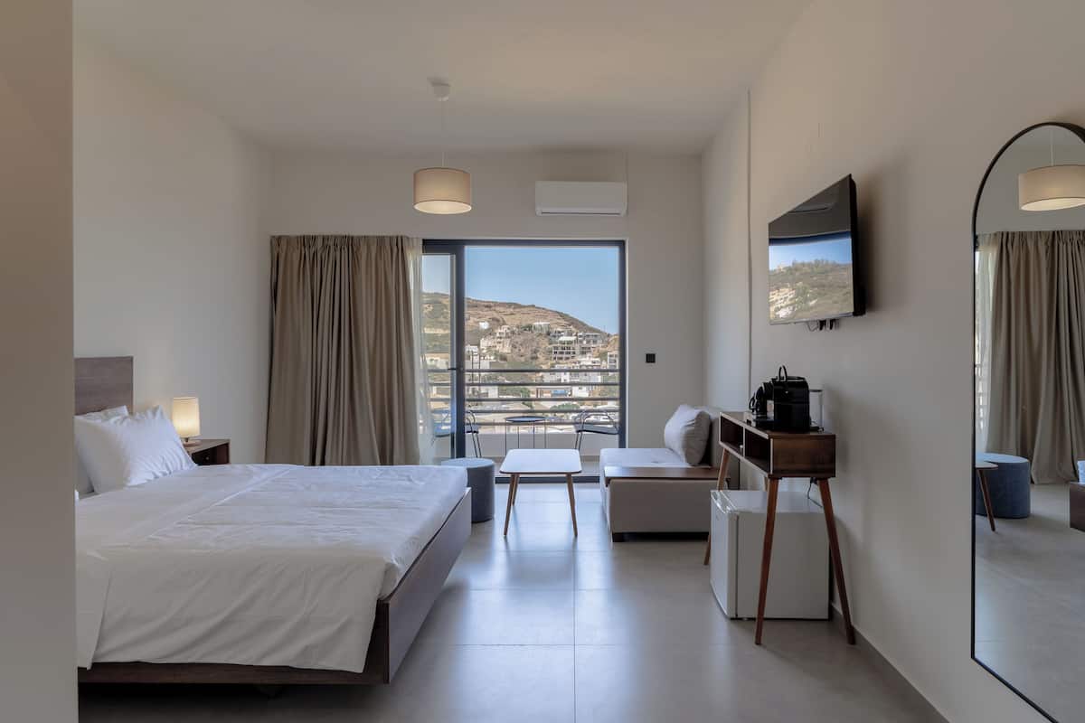 A hotel room with a large bed, a desk, a chair, a small table, a coffee machine, and a TV.