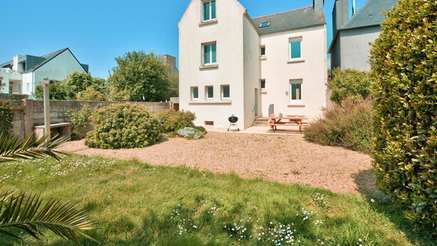 A two-story house with a sloped roof, a front porch, and a small garden area with a bench and grill. - House for 8 in the center of Plouguerneau (Plouguerneau)