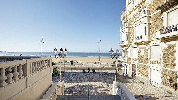 Un hotel con vista al mar, una terraza de madera y una escalera que baja a la playa.