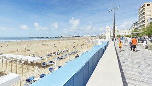 Una playa con tumbonas y sombrillas, un paseo marítimo con gente y edificios al fondo.