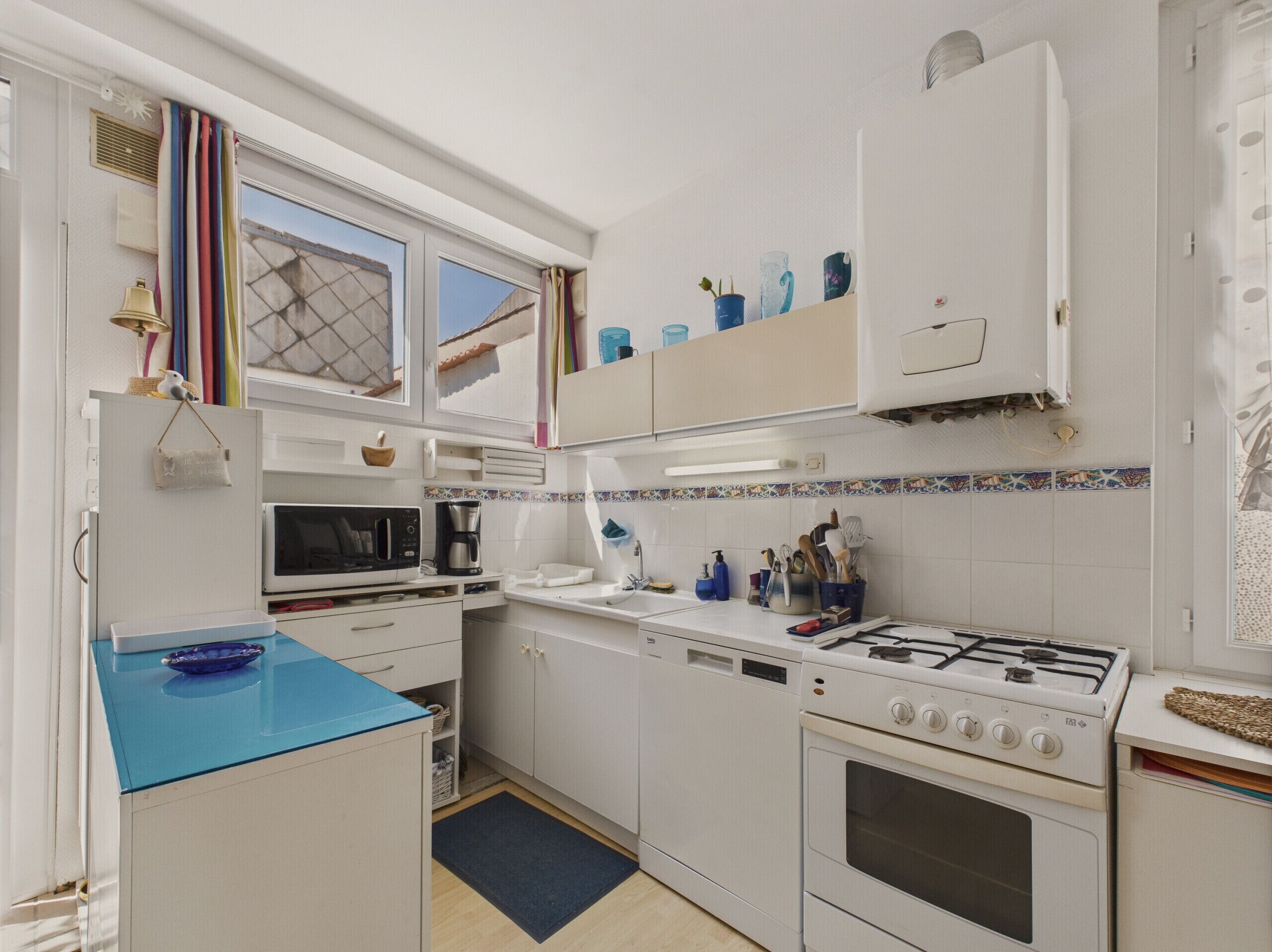 A compact kitchen with white cabinets, a blue countertop, a microwave, a coffee maker, a gas stove, and a dishwasher.