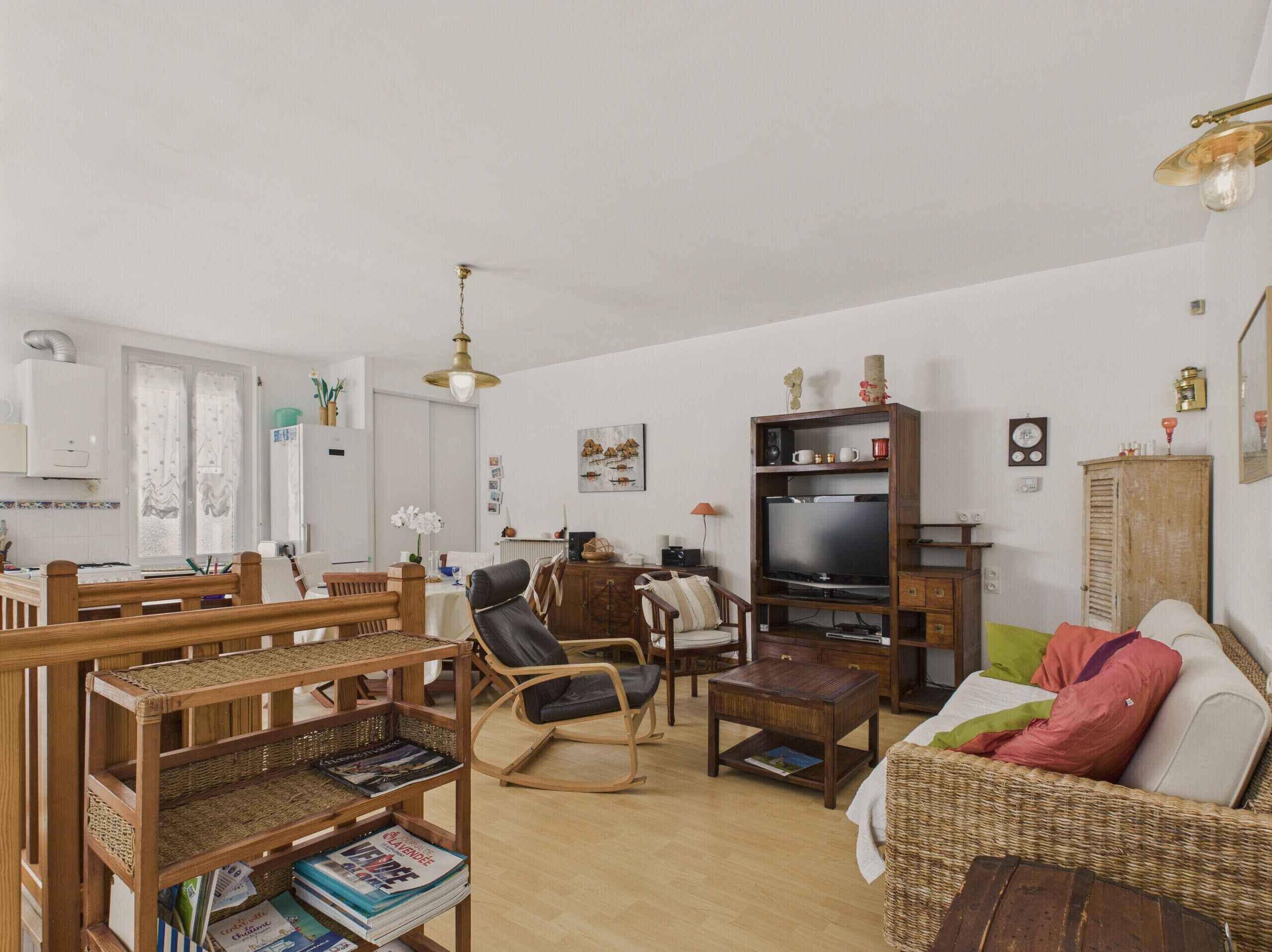 Een woonkamer met een televisie, houten meubels, een rieten bank en een eethoek met een tafel en stoelen.