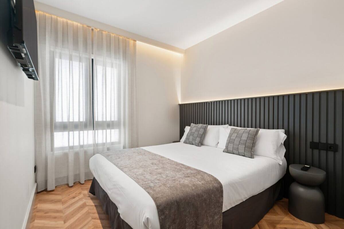 Une chambre moderne avec un grand lit, une table de chevet et un téléviseur fixé au mur.