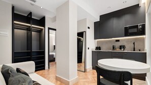 Una cocina moderna con armarios oscuros, microondas y cafetera. Hay una mesa de comedor blanca con un banco.
