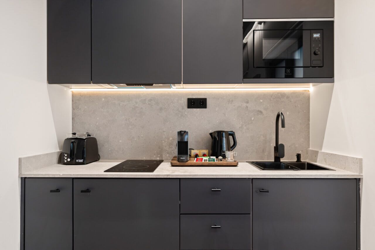 Una cocina moderna con armarios oscuros, microondas integrado, tostadora, cafetera y un lavabo.