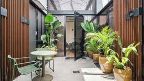 Un espacio interior moderno con puerta de cristal, plantas en macetas, una pequeña mesa con una silla y un cartel con el número 09 en la pared.