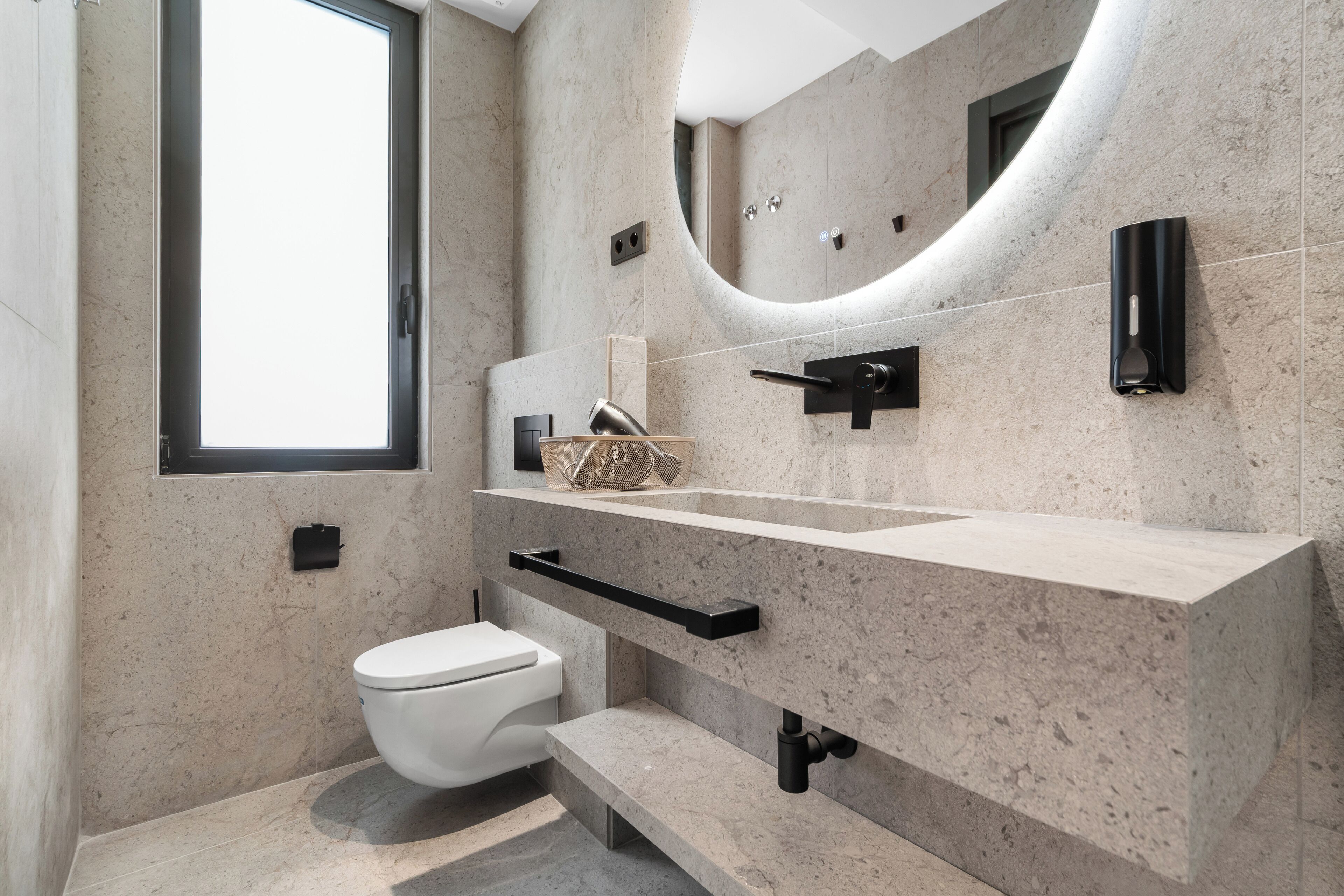 A modern bathroom with a white toilet, a large mirror, and a curved sink vanity.