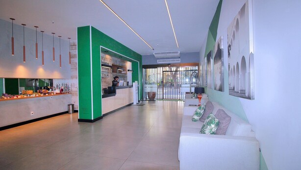 A modern reception area with a green accent wall, a counter with various items, and a seating area with a couch. - Conforto Localização Imbatível U054 (Rio de Janeiro)