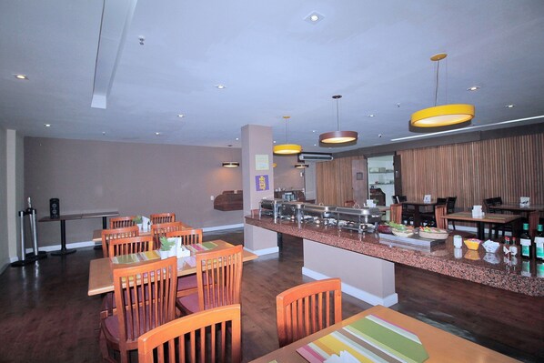 Comedor de hotel con mesas y sillas de madera, un mostrador de buffet e iluminación colgante.