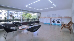A modern waiting area with black chairs, a small table, and a laundry station. - Conforto Localização Imbatível U054 (Rio de Janeiro)