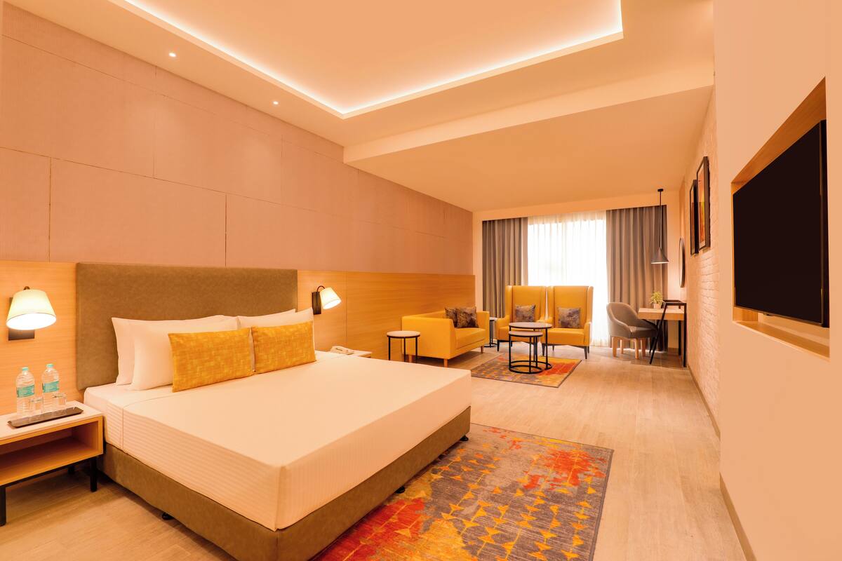 A hotel room with a large bed, bedside tables, a desk, a chair, and a TV.