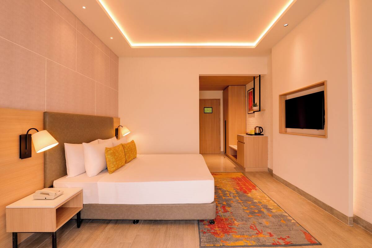 A modern hotel room with a large bed, bedside lamps, a flat-screen TV, and a small desk with a telephone.