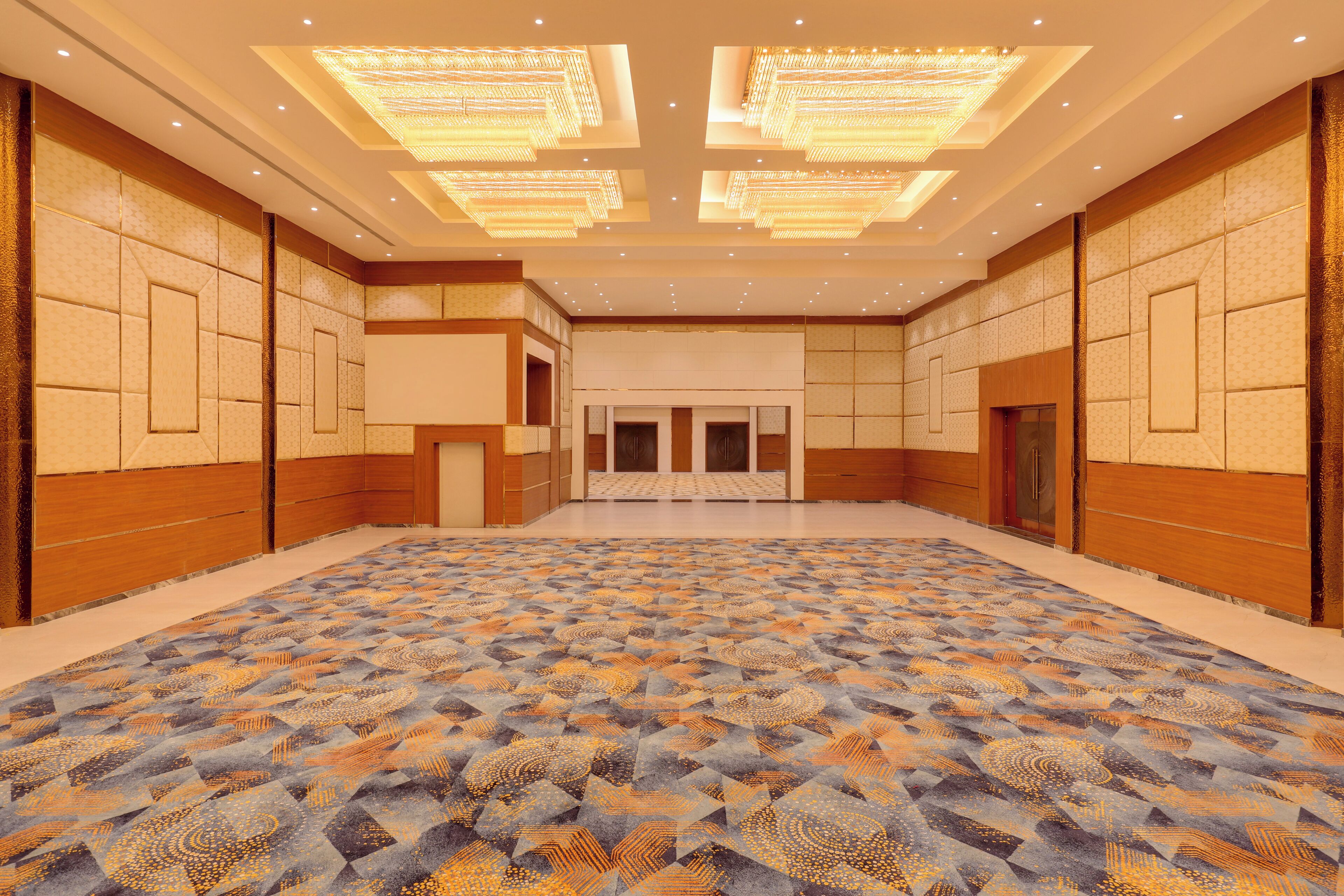 A spacious room with a patterned carpet, recessed lighting, and wooden paneling on the walls.