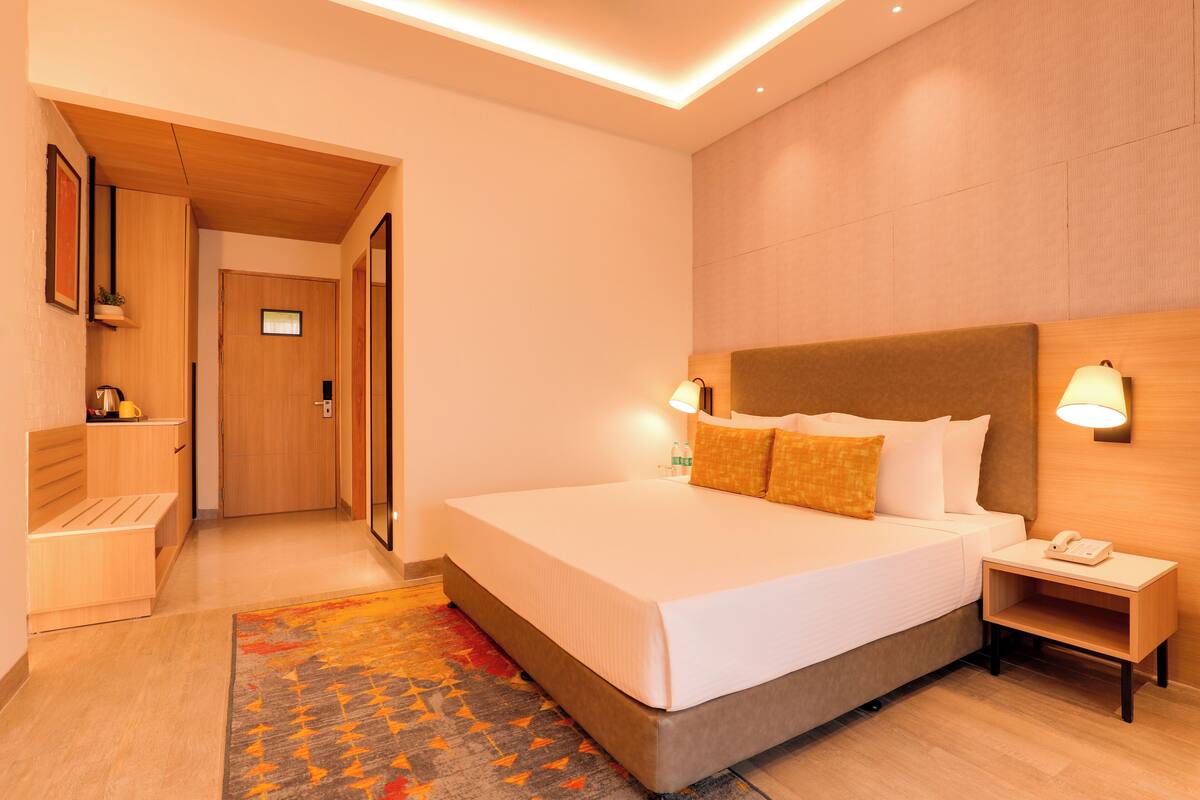 A modern hotel room with a large bed, bedside lamps, a wooden headboard, and a small bedside table with a phone.