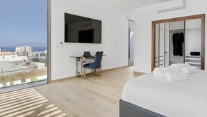 A modern hotel room with a large bed, a desk with a chair, a TV mounted on the wall, and a closet with a mirror. - Villa Élan (Playa Paraiso)