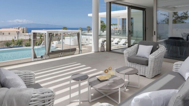 A modern balcony with a pool view, white wicker furniture, and a glass door leading to a terrace. - Villa Élan (Playa Paraiso)