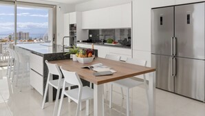 A modern kitchen with white cabinetry, a stainless steel refrigerator, and a dining area with white chairs and a wooden table. - Villa Élan (Playa Paraiso)