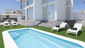 Ein modernes Haus mit einem Swimmingpool, weißen Liegestühlen und einer Treppe, die zum Eingang führt.