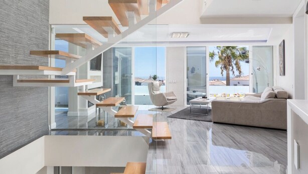 Ein modernes Interieur mit Treppe, einer Wohnbereicherung mit Sofa und Couchtisch sowie Blick auf den Strand.