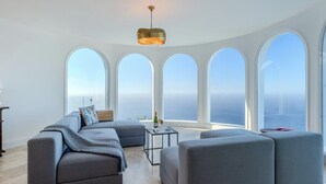 A modern living room with a sectional sofa, a coffee table, and a view of the ocean through large windows. - Villa Aurea (El Sauzal)