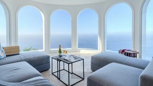 A modern living room with a large window overlooking the sea, a sofa set, a coffee table, and a small side table. - Villa Aurea (El Sauzal)