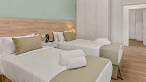 Hotellihuone, jossa on kaksi sänkyä, puinen sängynpääty, valkoiset vuodevaatteet ja vaatekaappi.