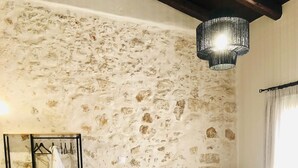 Een slaapkamer met een stenen muur, een bed met wit beddengoed, een hangstoel en een klein tafeltje met een fles.