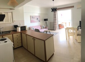 A modern kitchen with a central island, a dining area with a table and chairs, a sofa, and a large window with curtains. - Kate Apartment Across the Marina (Rethymno)