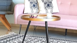 Un canapé rose agrémenté de coussins à motifs, une petite table ronde avec une théière et une tasse, et un tapis noir et blanc à motifs.