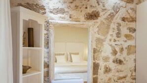 Quarto com parede de pedra, cama branca e cadeira branca.