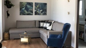 A modern living room with a grey sectional sofa, a blue armchair, a small round table, and two wall-mounted paintings of birds. - Areti Seaview Residence (Rethymno)
