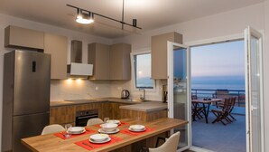 A modern kitchen with a wooden table set for dining, a refrigerator, and a view of the sea through a glass door. - Areti Seaview Residence (Rethymno)