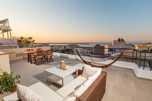 Eine Dachterrasse mit einer Hängematte, einer Sitzgelegenheit und Blick auf das Meer.