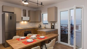 A modern kitchen with a wooden table set for dining, a built-in oven, and a view through a glass door to the outside. - Areti Seaview Residence (Rethymno)