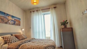 A bedroom with a bed, a painting, a window with curtains, and a plant. - Modern 3 Bedroom Penthouse With Rooftop Views (Msida)