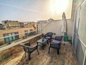 Ein Balkon mit Tisch und Stühlen, einem Blumentopf und Blick auf die Stadtlandschaft.