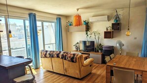 A modern living room with a sofa, TV, dining table, and chairs. - Modern 3 Bedroom Penthouse With Rooftop Views (Msida)