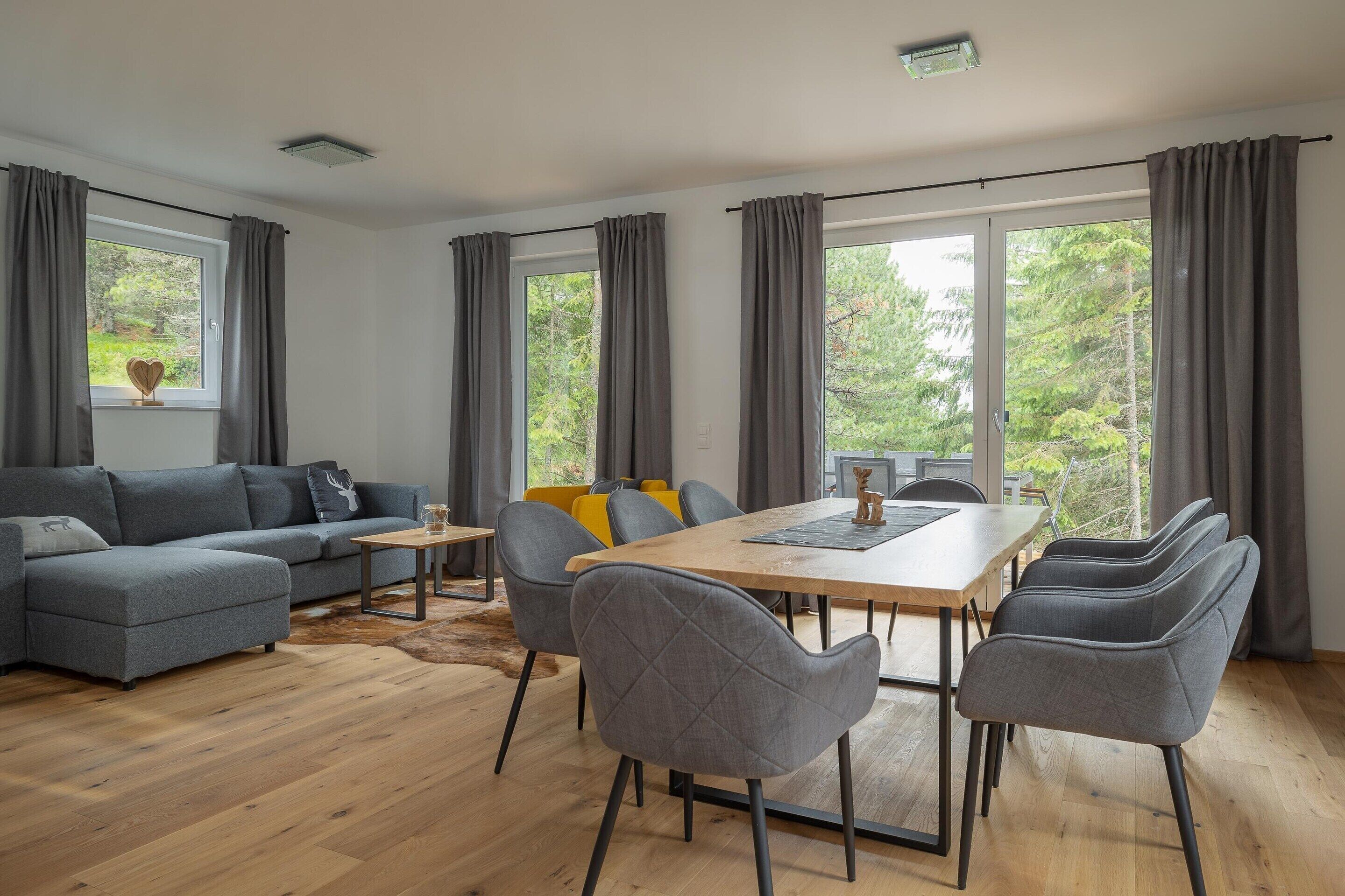 A modern living room with a grey sofa, a wooden dining table, and grey chairs.