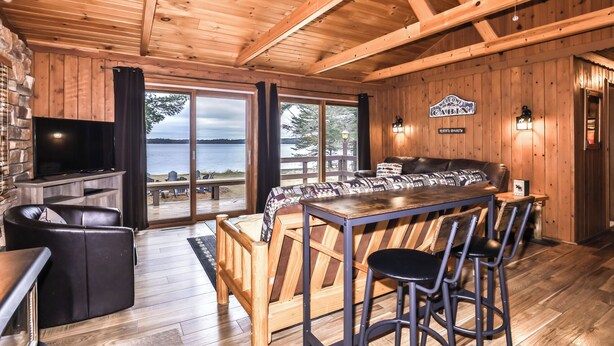 Une cabane avec un intérieur en bois, un coin bar, un téléviseur et une vue sur un lac.
