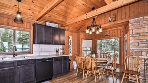 L’intérieur d’un chalet en bois comprend une cuisine, un coin repas et de grandes fenêtres donnant sur une zone boisée.