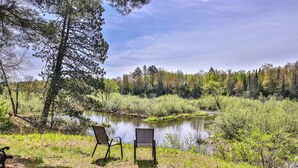 A serene lakeside setting with two chairs facing the water, surrounded by lush greenery and trees. - Stepaway Vacation Rentals- Happy Hours Pet Friendly (Eagle River)